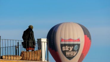 a man standing on a balcony next to a hot air balloon